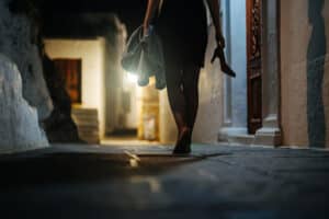 Woman walks home barefoot at night after a party.